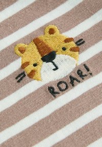 Pruhovaná látka v béžovej a bielej farbe s vyšitým tigrom a nápisom "ROAR!" v čiernej farbe. Tiger má žlté a hnedé akcenty.