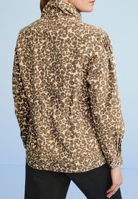 Leopard print shirt with a high collar, made of lightweight fabric, featuring pleated shoulders and buttoned cuffs in neutral tones.