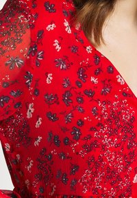 Rotes Kleid mit floralem Muster und kurzen, transparenten Ärmeln. Verziert mit komplizierten lila und weißen Blumen auf einem strukturierten Hintergrund. V-Ausschnitt-Design.