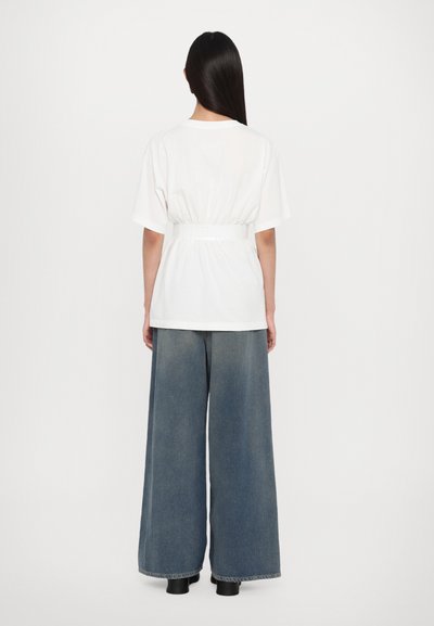 Vit kortärmad topp med samlad midja, tillsammans med vida blå denimbyxor. Slät textur, avslappnad passform och minimalistisk design.