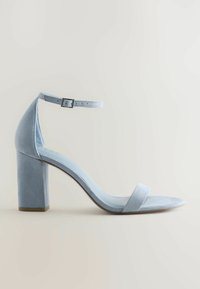 Sandale à talon haut en daim bleu clair avec bride à la cheville, fermeture à boucle et talon bloc, présentée sur un fond neutre.