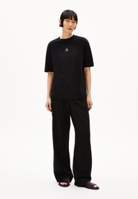 Zwart T-shirt met korte mouwen en een klein wit logo, gecombineerd met losse zwarte broek en donkere sandalen, allemaal gemaakt van zachte stof.