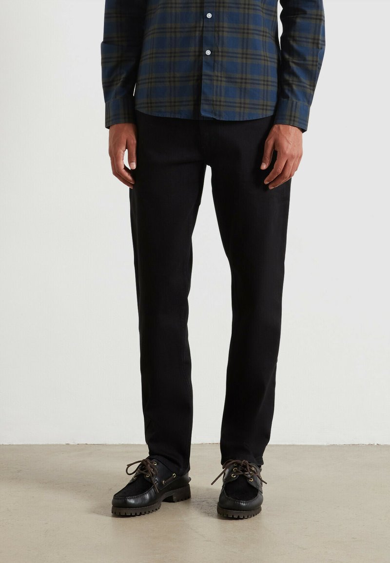 Pantaloni neri con design a gamba dritta, realizzati in un tessuto testurizzato, abbinati a scarpe nere con una suola robusta e lacci.