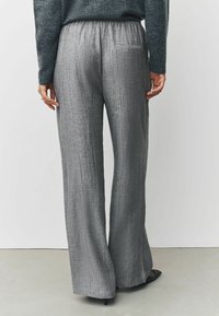 Graue, weite Hosen mit einem strukturierten, zerknitterten Stoff. Verfügt über einen elastischen Bund und eine einzelne Gesäßtasche.