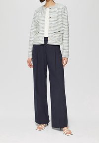 Light blue tweed jacket with gold buttons, paired with dark navy wide-leg trousers and white strappy sandals, creating a tailored look.