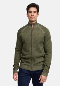 Groene trui met ritssluiting, hoge kraag, gebreide structuur en bruine ritssluiting als accent. Geribbelde manchetten en zoom, aansluitend model.