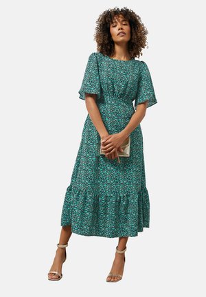 Groene bloemen midi-jurk met korte fladdermouwen, een cinched taille en een gelaagde ruffelzoom. Gecombineerd met een metallic clutch en sandalen met bandjes.