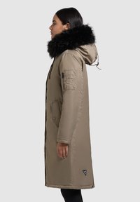 Khaki parka jakk, millel on eemaldatav must kunstkarvane kapuuts, eesnep zipp, külgmised taskud ja aktsentplekk alumisel serval.