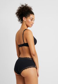 Reggiseno nero e slip a vita alta abbinati. Il reggiseno presenta spalline regolabili e chiusura a gancio; gli slip hanno un bordo in pizzo. Tessuto con una texture liscia.