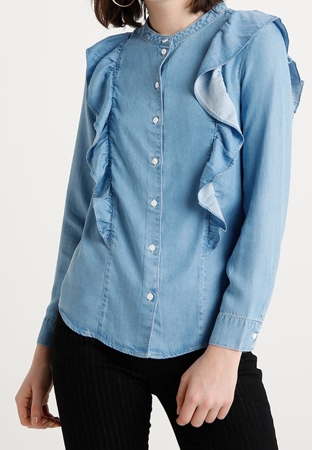 Camicia in denim azzurro chiaro con dettaglio arricciato sul davanti, scollo rotondo e chiusura con bottoni. Presenta maniche lunghe e una vestibilità rilassata.