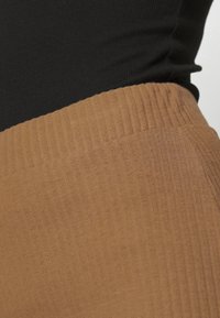 Hnědé žebrované legíny s elastickým pasem, zobrazené vedle černého přiléhavého topu. Tkanina má jemnou strukturu a slabý lesk.