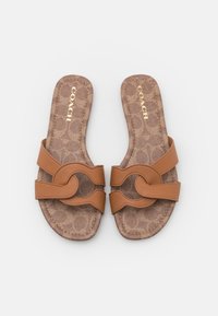 Brune Coach-sandaler med et struktureret mønster, dobbelte stropper med en cirkulær detalje og en flad sål. Guldlogo på indersålen.