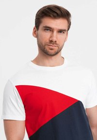 Camiseta de algodón con un diseño de bloques de color en secciones blanca, roja y azul marino. Manga corta, escote redondo y una textura suave.