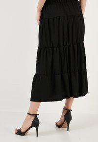 Black tiered midi skirt with an elastic waistband, paired with black high-heeled sandals featuring ankle straps and open toes.