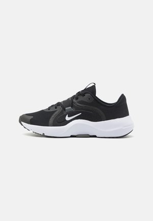 Sort atletisk sko med en åndbar tekstiloverdel, polstret krave, hvid mellemsål og en struktureret gummiydersål. Nike-logo i hvid.