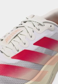 Κοντινή λήψη λευκού και κόκκινου παπουτσιού τρεξίματος Adidas Adizero με λευκά κορδόνια και ελαφρύ πάτο.