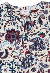 Blouse crème à motifs floraux avec des fleurs bleues, rouges et violettes, dotée d'un col rond avec un lien à l'avant et une étiquette de marque "CECIL".