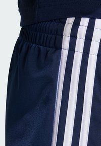 Granatowe sportowe spodenki z białymi paskami po bokach, elastycznym pasem i gładką, lekką fakturą materiału.