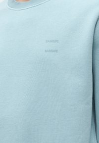 Ανοιχτό μπλε φούτερ με στρογγυλή λαιμόκοψη και διακριτικό ανάγλυφο κείμενο "SAMSOE" στο στήθος, που δείχνει την υφή του υφάσματος και τις λεπτομέρειες της ραφής.