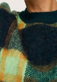 Gebreide trui met een mix van groene, oranje en marineblauwe ruitmotieven, met een zachte textuur en een ronde halslijn.