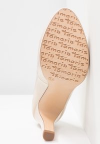 Semelle de chaussure à talon haut beige avec un motif de texte "Tamaris" répété et une indication de taille 37 sur la surface inférieure.