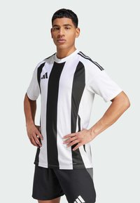 Wit en zwart gestreept sportshirt met korte mouwen, voorzien van een logo op de linkerkant van de borst en ademend materiaal. Gecombineerd met zwarte shorts.
