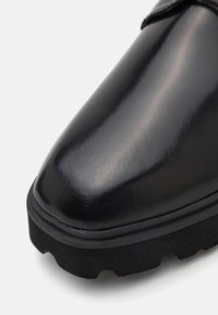 Botte en cuir noir poli avec un bout arrondi et une semelle épaisse en caoutchouc texturé, présentée en gros plan sur fond blanc.