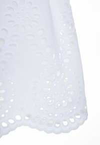 Tela blanca bordada con recortes circulares, que presenta un patrón de paisley y un borde con forma de concha. Textura suave y ligera.