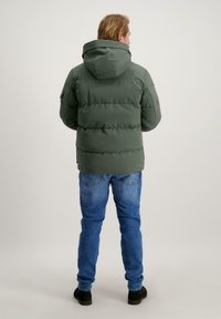 Groene pufferjack met capuchon, voorzien van een gewatteerd ontwerp, elastische manchetten en zichtbare stiksels. Gekocht met blauwe denim jeans en zwarte schoenen.