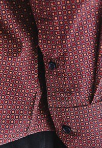 Koszula zapinana na guziki w kolorze maroon z geometrycznym wzorem w odcieniach pomarańczowym i żółtym. Czarne guziki widoczne z przodu.