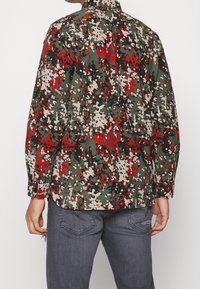 Camo-gepatroneerd shirt in groen, rood en beige, gemaakt van stof met een iets gestructureerde afwerking. Heeft lange mouwen en een kraag.