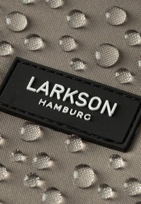 Šedá textúrovaná tkanina s vodnými kvapkami, s čiernym obdĺžnikovým logo nášivkou, na ktorej je v bielej farbe napísané "LARKSON HAMBURG".