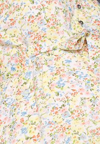 Vestido floral com uma palete de cores pastel, adornado com pequenas flores rosas, azuis e amarelas sobre um fundo claro. Inclui botões e um detalhe de laço.