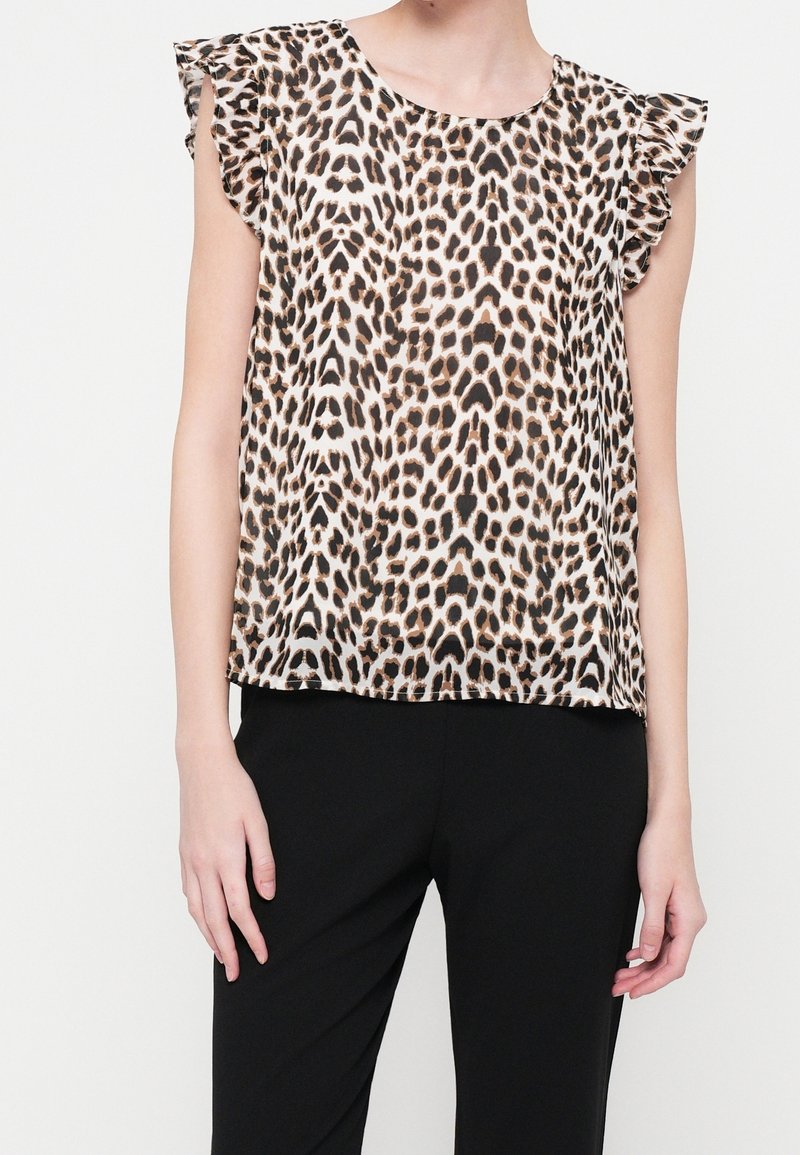 Blouse sans manches à imprimé léopard marron et noir avec manches courtes volantées, portée avec un pantalon noir.