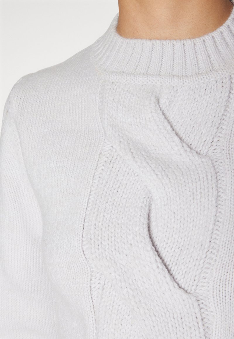 Maglione bianco lavorato a maglia con collo a costine e motivo a treccia testurizzato. Tessuto morbido e spesso con dettagli di cucitura visibili.