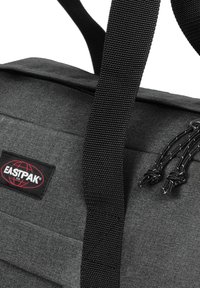 Borsa in tessuto grigio con logo nero, dotata di spallacci neri spessi e dettagli con coulisse. Texture liscia con design strutturato.