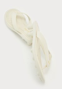 White flip-flops with a textured sole, featuring cross straps, a cushioned footbed, and gold branding on the insole.