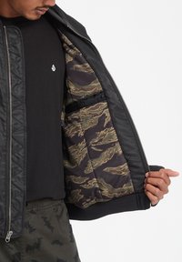 Giubbotto bomber nero con texture trapuntata, zip argento e fodera a motivo mimetico in tonalità di verde e marrone. Maniche e orlo regolabili.