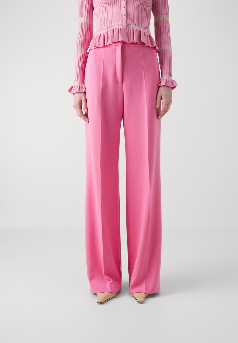 Pantalons larges roses en tissu lisse, avec taille haute, devant plissé et coupe décontractée. Associés à un haut à rayures roses.