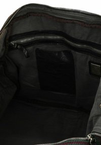 Interno di una borsa in tessuto nero con una tasca con zip, una patch in pelle liscia e un rivestimento in nylon con un dettaglio di bordo testurizzato.