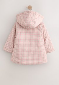 Veste à capuche à carreaux roses et blancs, manches longues, avec une texture matelassée et un ourlet arrondi. Suspendue à un crochet en bois.