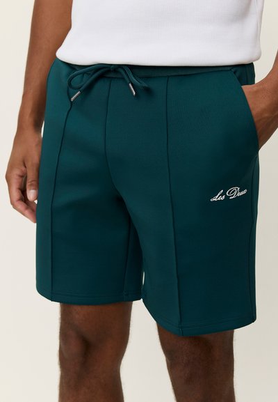 Shorts de sport bleu sarcelle foncé en tissu lisse, avec une taille élastique, un cordon de serrage, des poches latérales et un logo brodé blanc.