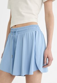 Pantaloni corti azzurri realizzati in tessuto morbido, con cintura elasticizzata, cordoncino e spacchi laterali per facilitare i movimenti.