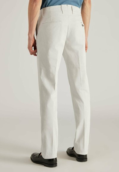 Weiße Hosen aus einem strukturierten Stoff, mit klassischem Schnitt, Gesäßtaschen und einem glatten Bund. Getragen mit schwarzen Schuhen.