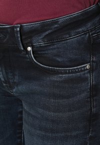 Jeans azul oscuro con una textura suave, que presentan un diseño clásico de cinco bolsillos y acentos de hardware plateado en los bolsillos.