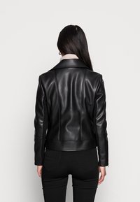 Giacca di pelle nera con un design aderente, spalle strutturate e cuciture visibili. Presenta un orlo dritto e una texture liscia.