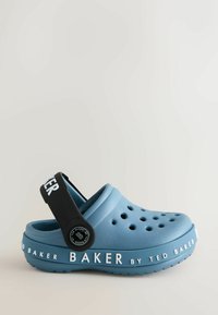 Modré gumové klumpa s ventilačnými otvormi, čierny akcentový popruh a bielym označením "TED BAKER" pozdĺž podrážky. Uzavretý dizajn.