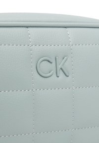 Borsa in pelle trapuntata azzurro chiaro con logo "CK" in rilievo e cuciture bianche a contrasto. Presenta una finitura liscia e una forma strutturata.