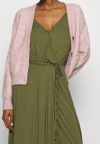 Light pink fuzzy cardigan with long sleeves over an olive green wrap dress featuring a cinched waist and V-neckline.