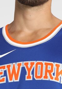 Blå baskettröja med "NEW YORK" i fet orange bokstäver. Rund halsringning med orange och vit kant; Nike-logotyp på vänster sida.